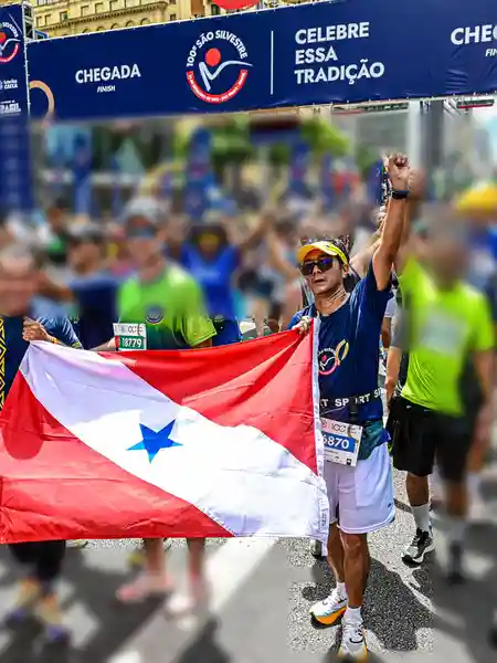 Mauricio Bezerra de Sousa com a bandeira do Pará sob o pórtico de chegada da 100ª São Silvestre